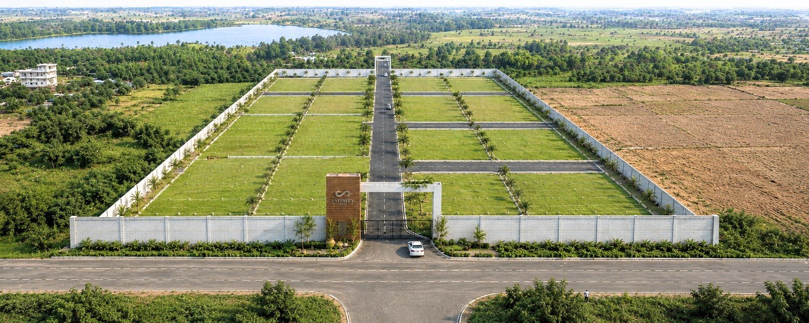 Aerial view of Infinity Town gated villa plot layout in Mahabalipuram, showing compound wall, blacktop internal roads and demarcated plots at Poonjeri, ECR